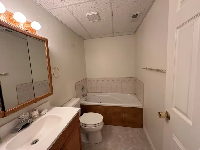 Bathroom featuring a corner jetted tub with tiled surround, a vanity with an integrated sink and wood-finish cabinetry, a framed mirrored medicine cabinet, and overhead lighting
