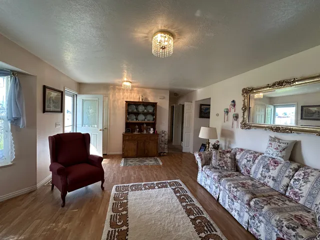 Open living area featuring wood-finish flooring, two crystal-style ceiling light fixtures, a white entry door with decorative glass, and a built-in wood hutch