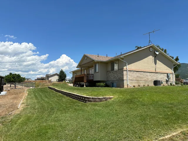 Spacious backyard featuring a sloped lawn, a multi-level retaining wall, and a raised wooden deck