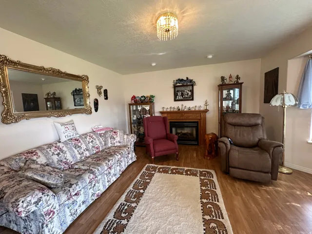 Living area featuring wood-finish flooring, a fireplace with a wood mantel, and a prominent chandelier