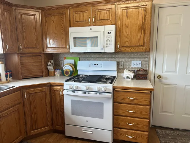 Oak cabinetry with gold-toned hardware, white solid surface countertops, and a full tile backsplash