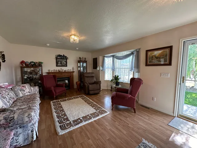 Spacious living area featuring wood-finish flooring, a bay window with natural light, and a fireplace with a wood mantel