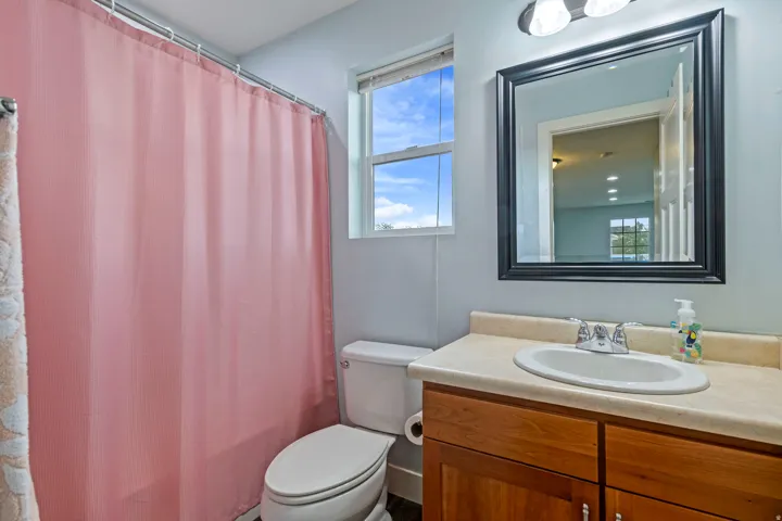 Bathroom featuring a single-sink vanity with wood-finish cabinetry, a light-toned countertop, and a framed mirror