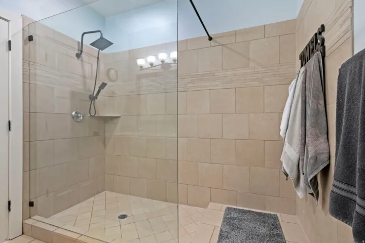 Walk-in shower featuring clear glass enclosure, neutral large format wall tiles, a decorative accent tile band, black-finish overhead rain shower, and an integrated shower niche