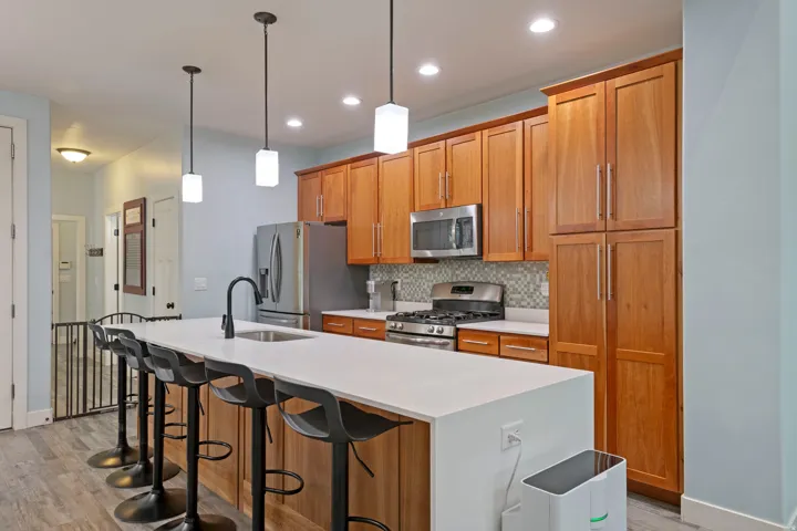 Contemporary kitchen featuring a large island with integrated sink, wood-finish cabinetry, stainless steel appliances, and pendant lighting