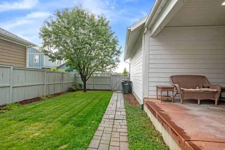 Private backyard featuring a paved stone walkway, manicured lawn, and a mature shade tree