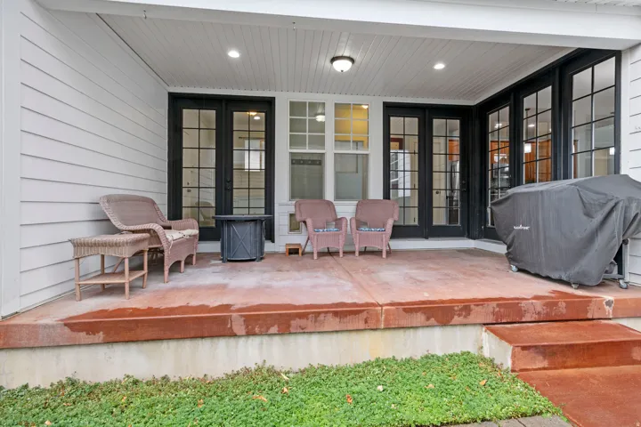 Covered patio featuring a concrete surface with two steps, black-framed French doors, additional transom windows, and white siding