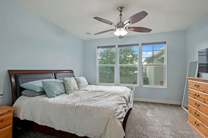 Bedroom featuring a vaulted ceiling, three windows, overhead ceiling fan with light fixture, and carpet flooring