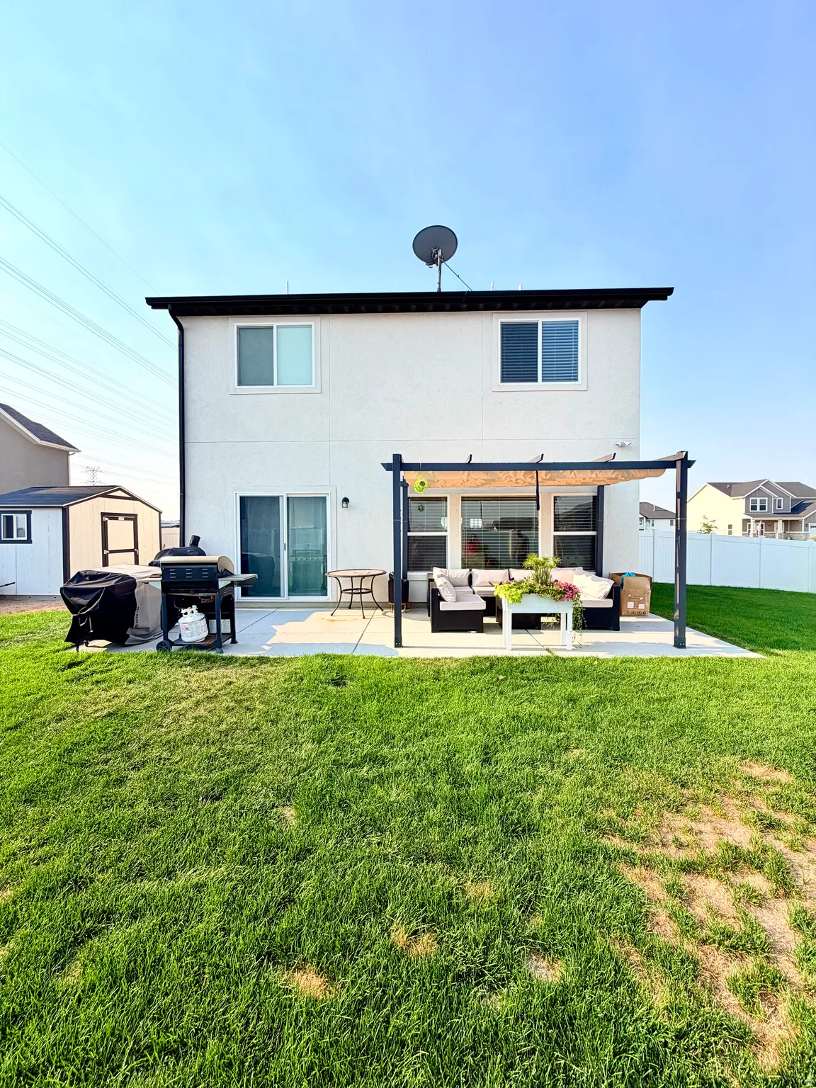 Rear exterior featuring a ground-level patio, white siding, and a black pergola structure