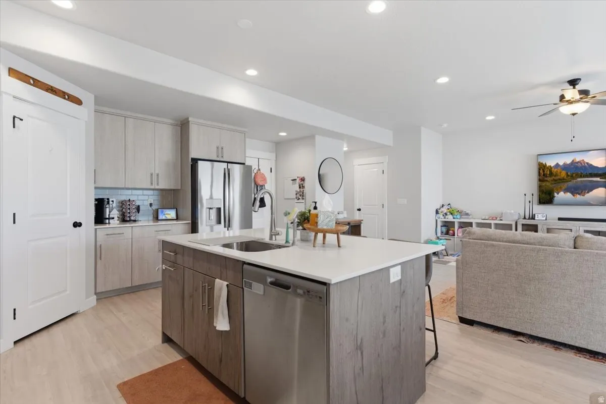 Open-concept kitchen featuring an island with an integrated sink and dishwasher, light-toned wood-finish cabinetry, stainless steel refrigerator, and recessed lighting