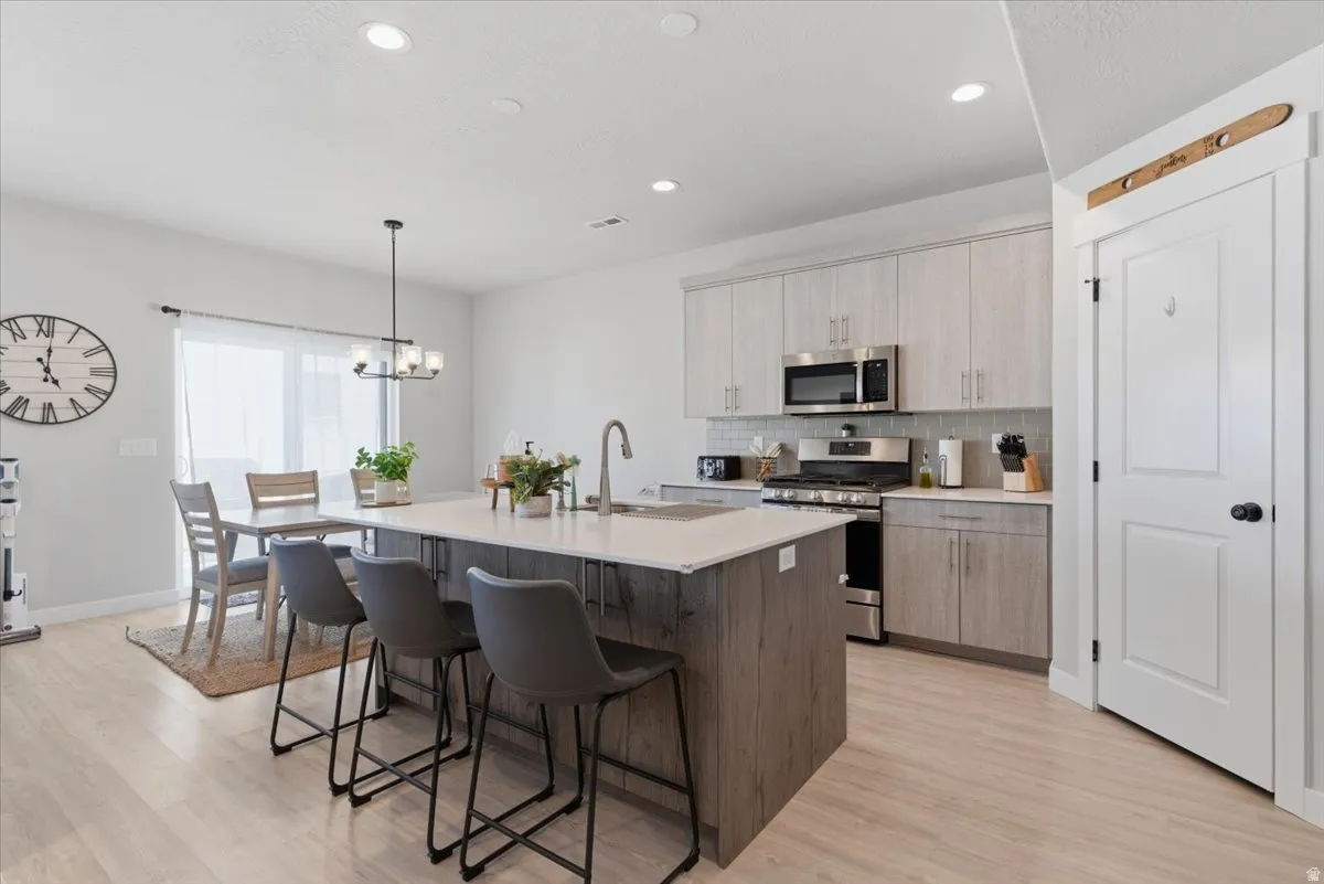 Open-concept kitchen featuring a central island with countertop seating, light wood-finish flooring, recessed lighting, stainless steel appliances, and light-toned cabinetry