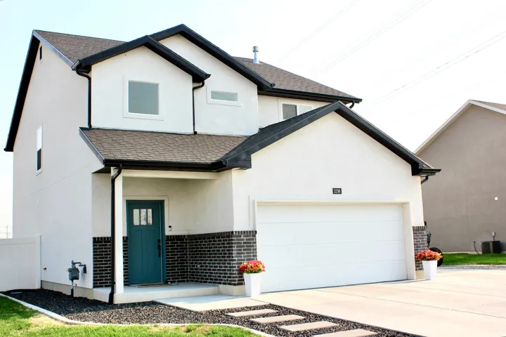 Modern two-story residence featuring a crisp white exterior with contrasting black architectural trim, brick veneer detailing at the foundation, and a two-car garage with white paneled door