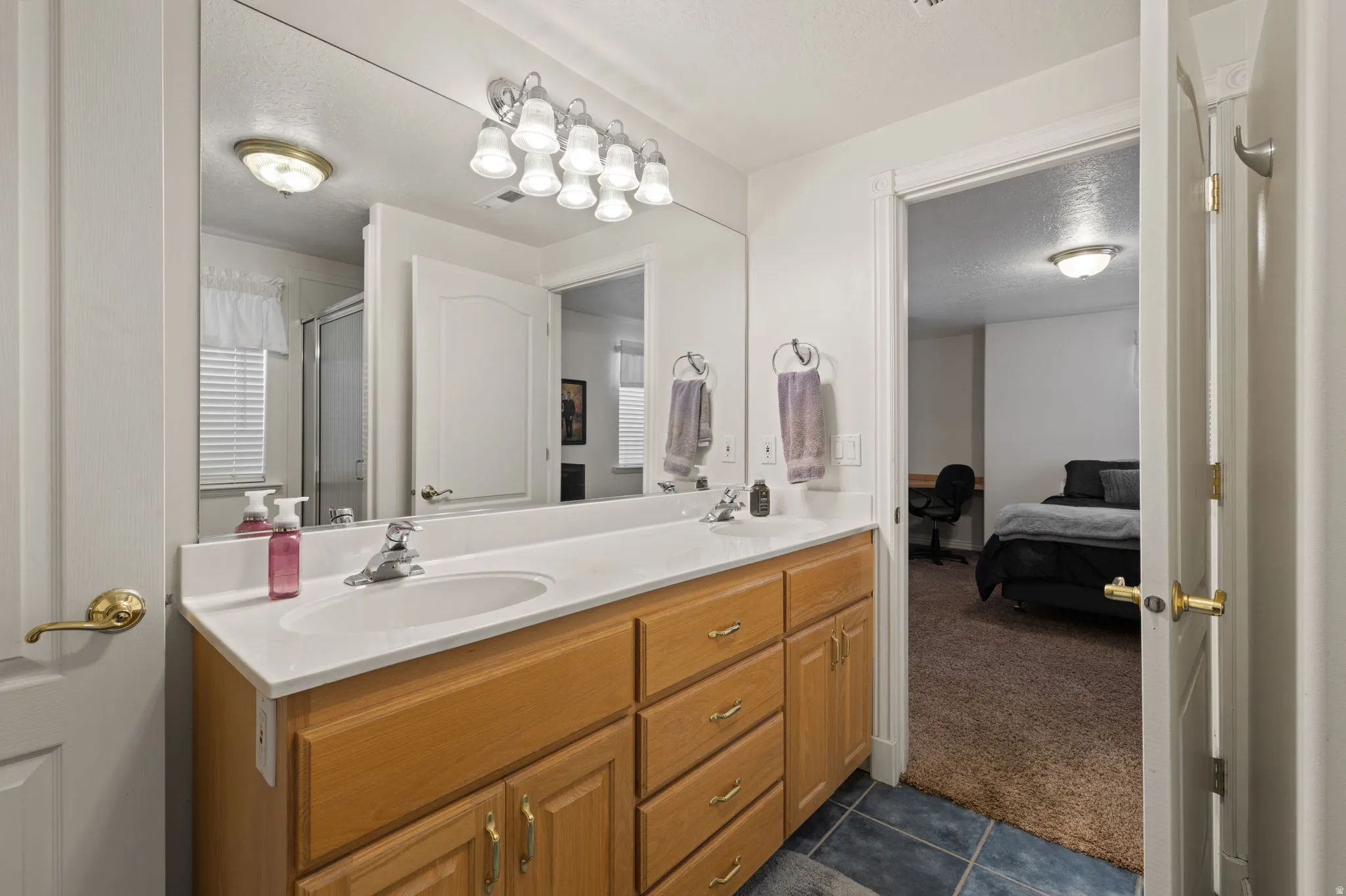 Bathroom featuring a dual sink vanity with a light wood-finish cabinet, a large frameless mirror, and overhead vanity lighting
