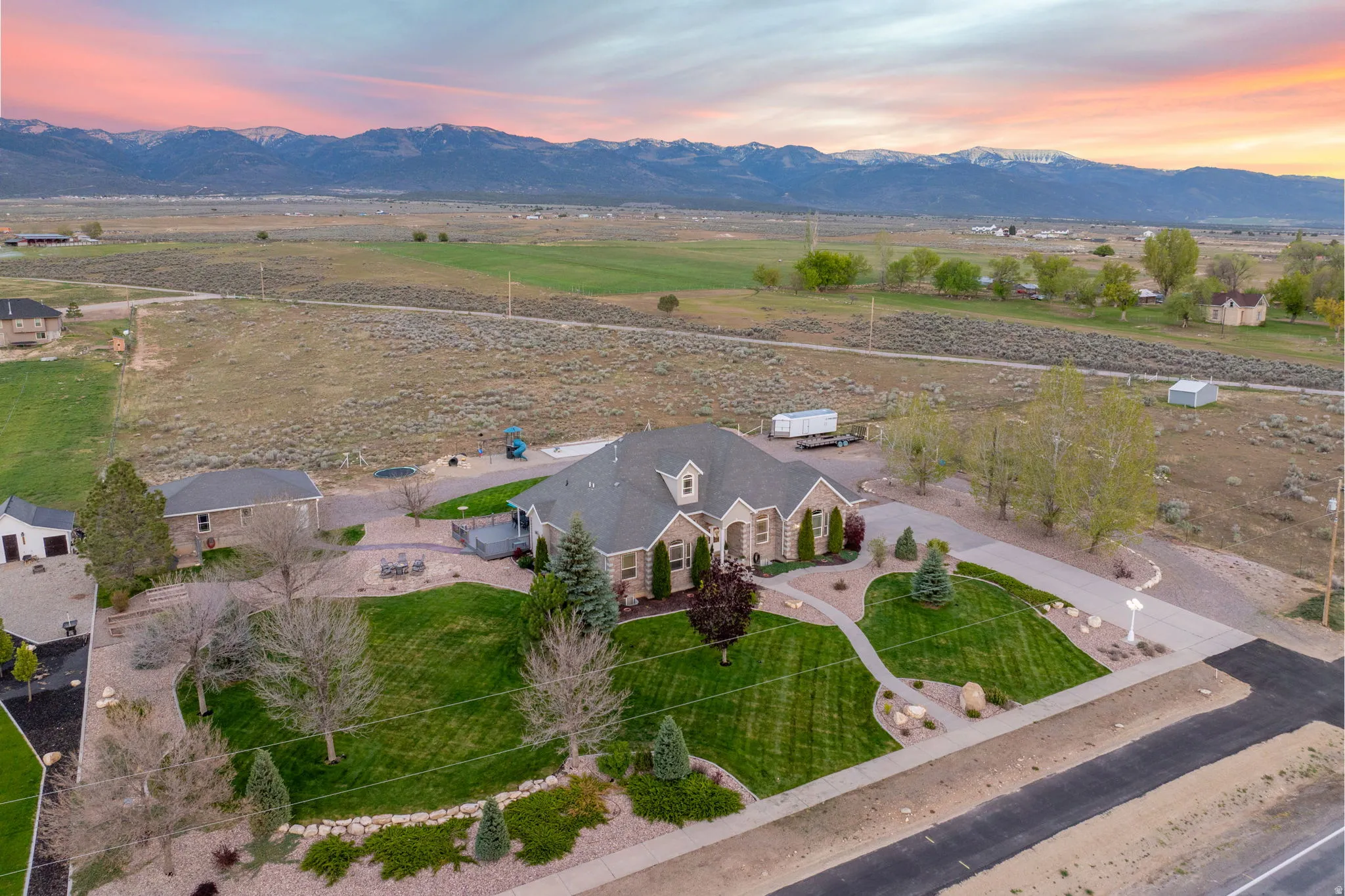 Spacious property featuring a large residence with a stone and siding exterior, a manicured lawn, an extended driveway, and a detached structure
