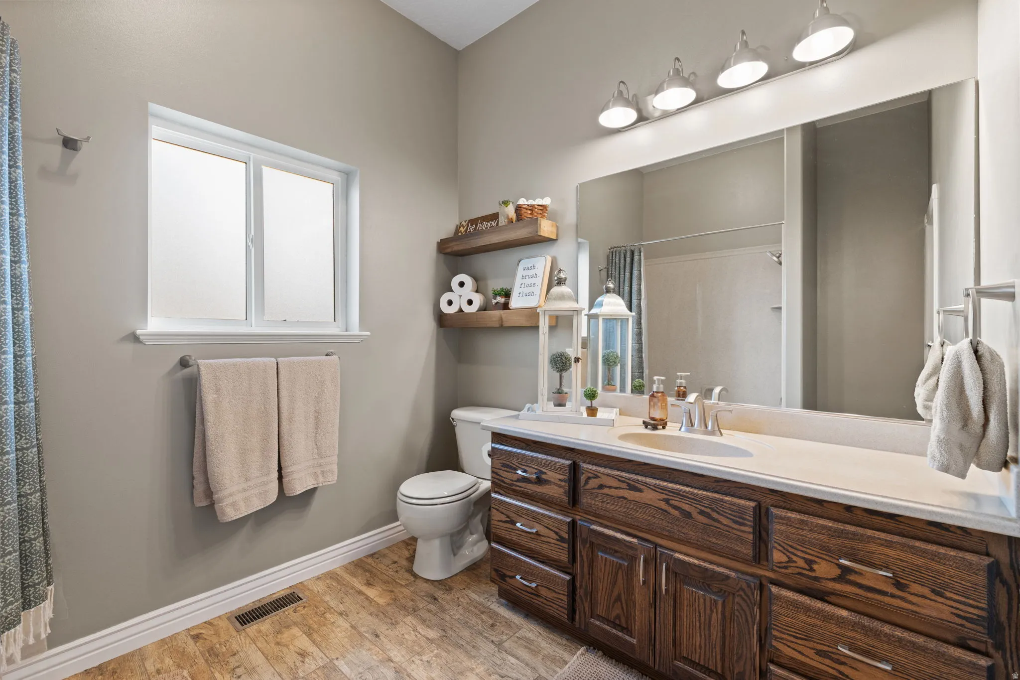 Bathroom featuring a wood-finish vanity with ample storage, a white countertop, and a large wall-mounted mirror