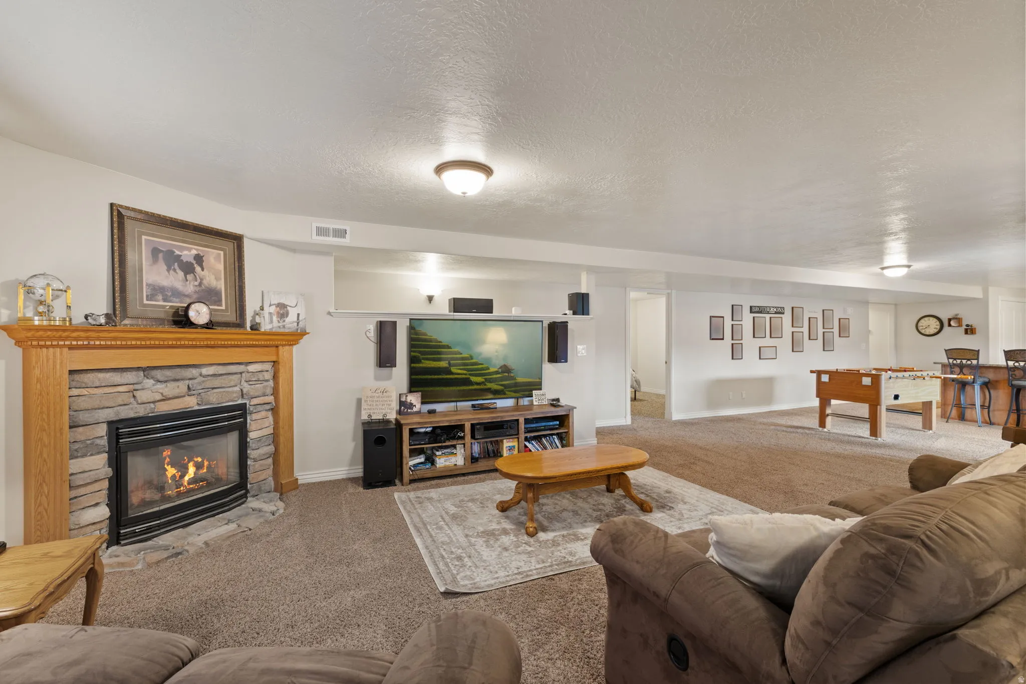 Spacious lower level featuring a stone-surround fireplace with a wood mantle, recessed lighting, and durable carpet flooring
