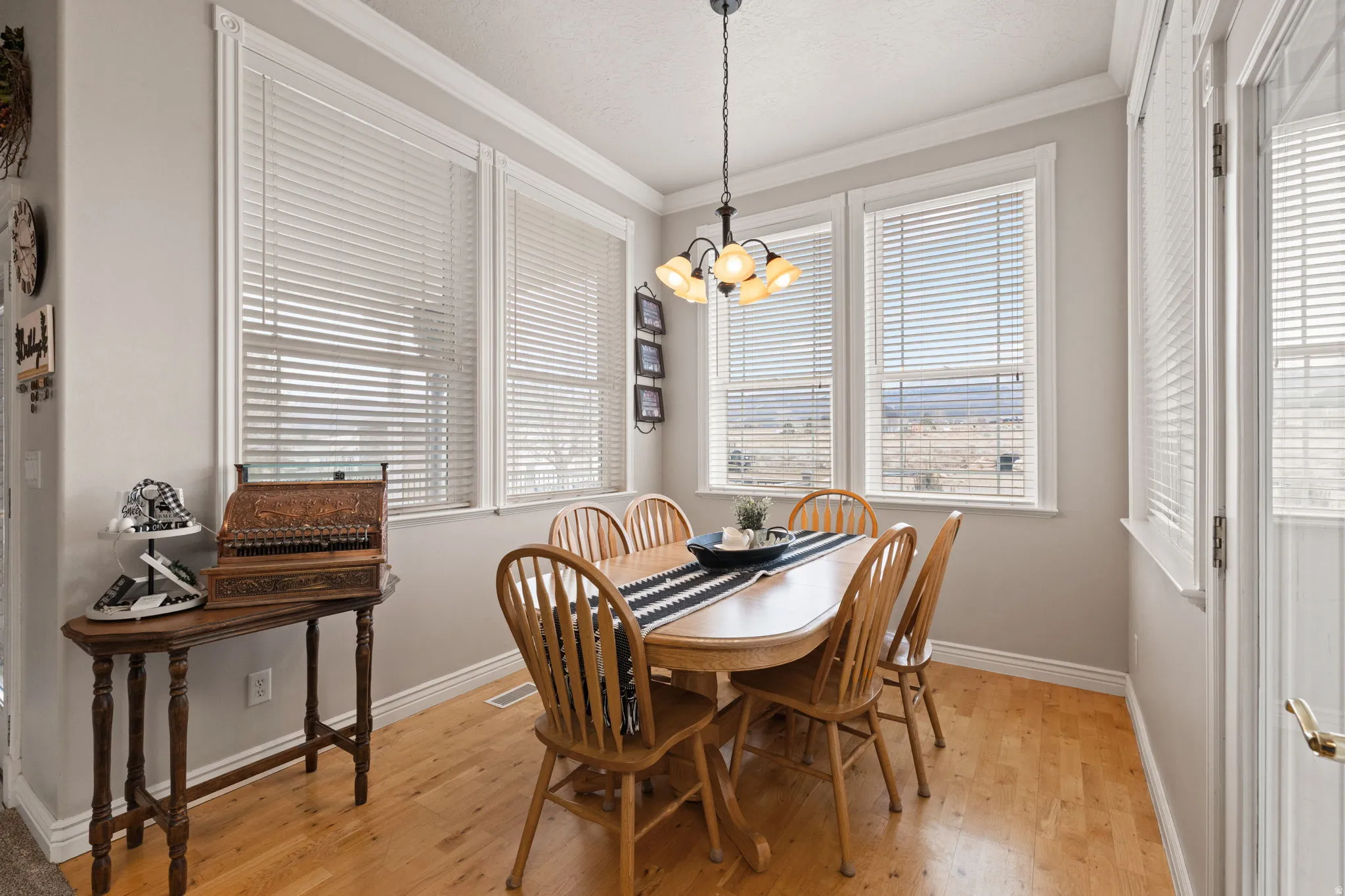 Dining area with wood-finish flooring, ample natural light through multiple windows, crown molding, and a five-light chandelier