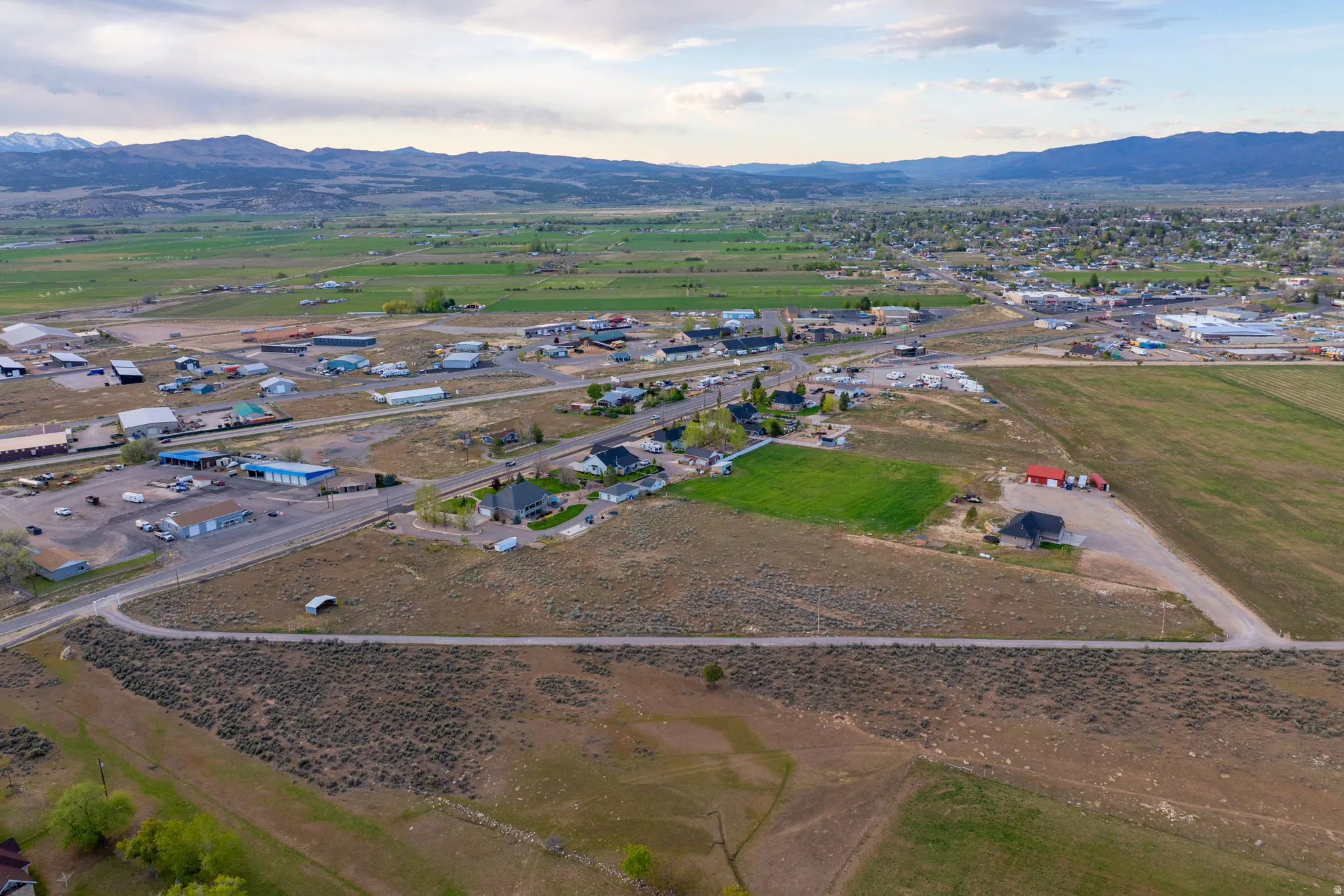 Expansive rural landscape featuring a mix of open fields, developed areas, and distant mountains under a cloudy sky