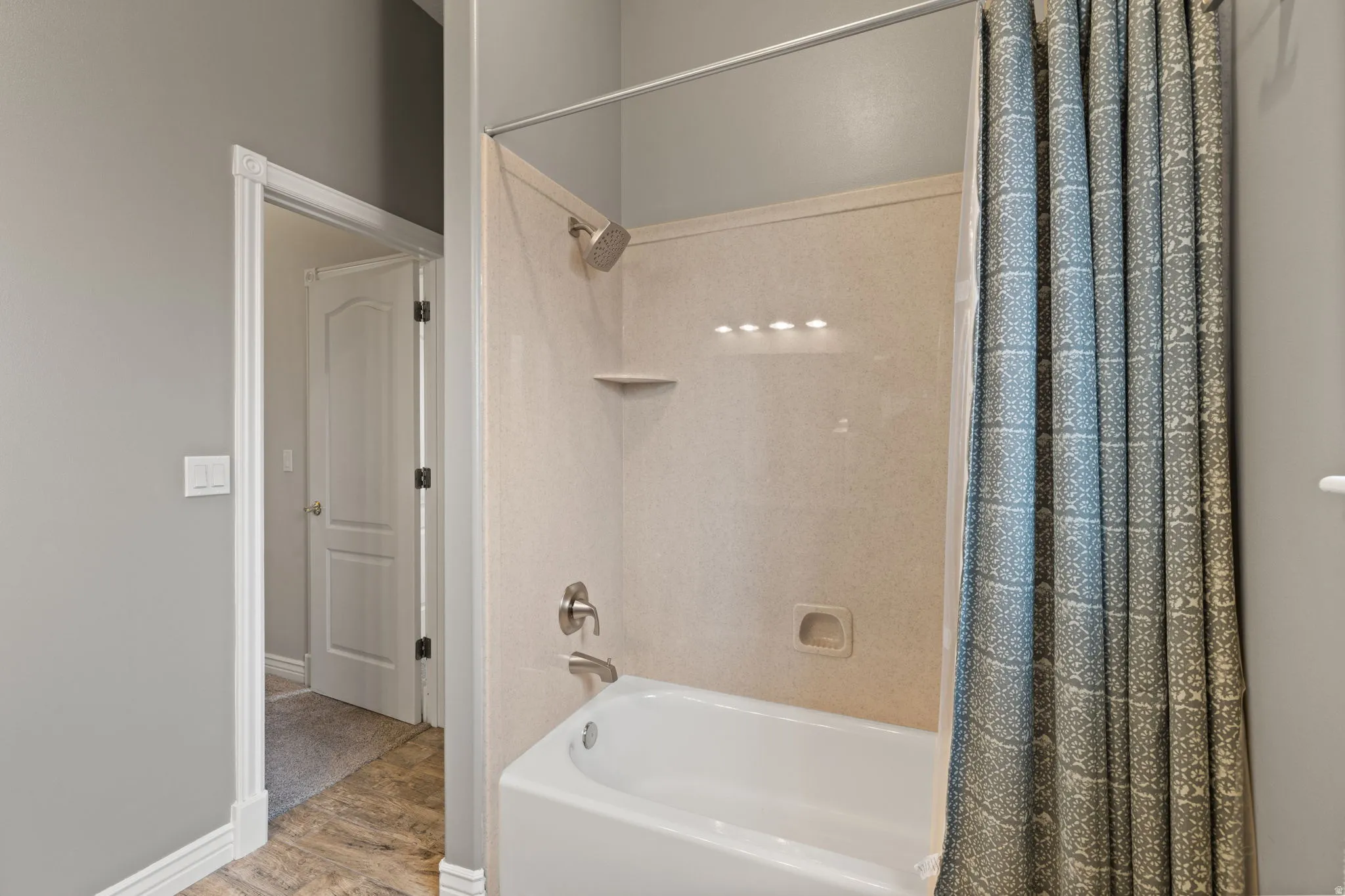 Bathtub and shower combination featuring a brushed nickel showerhead and faucet, integrated soap dish, and overhead lighting