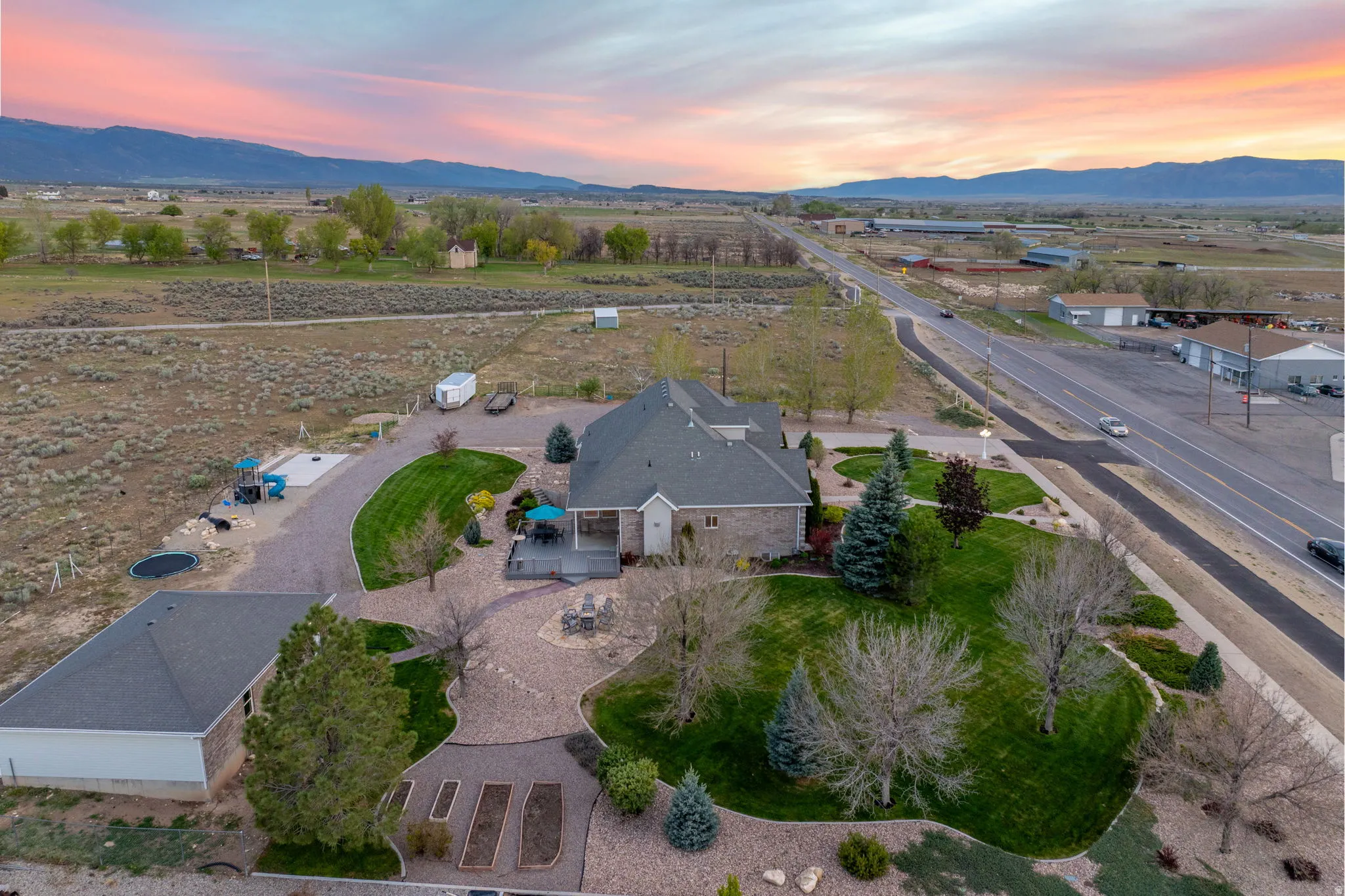 Aerial property overview featuring a main residence with a covered patio, a detached garage, and a gravel driveway