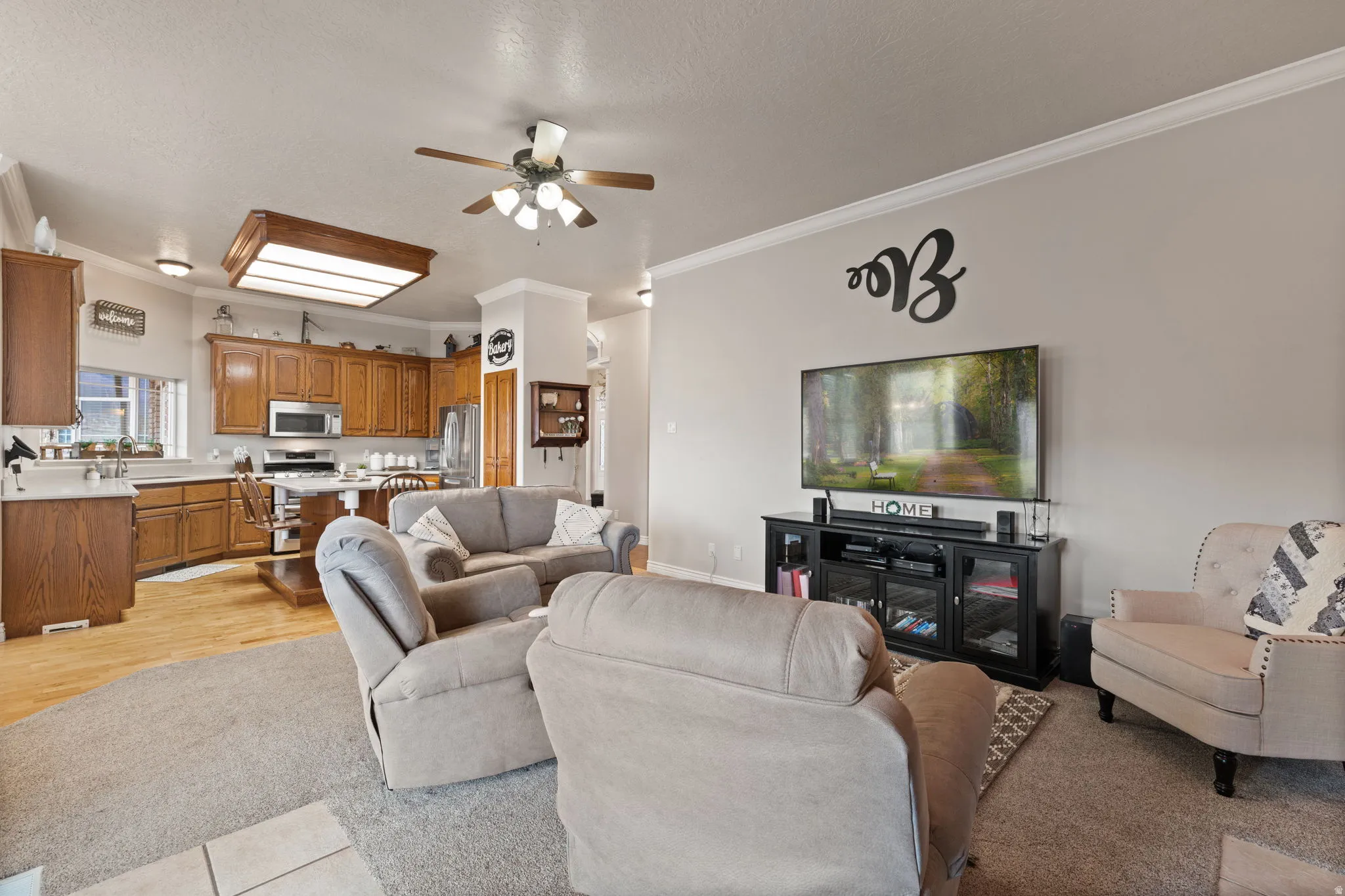 Open-concept living space featuring a kitchen with wood cabinetry and stainless steel appliances, a breakfast bar, and light wood-finish flooring