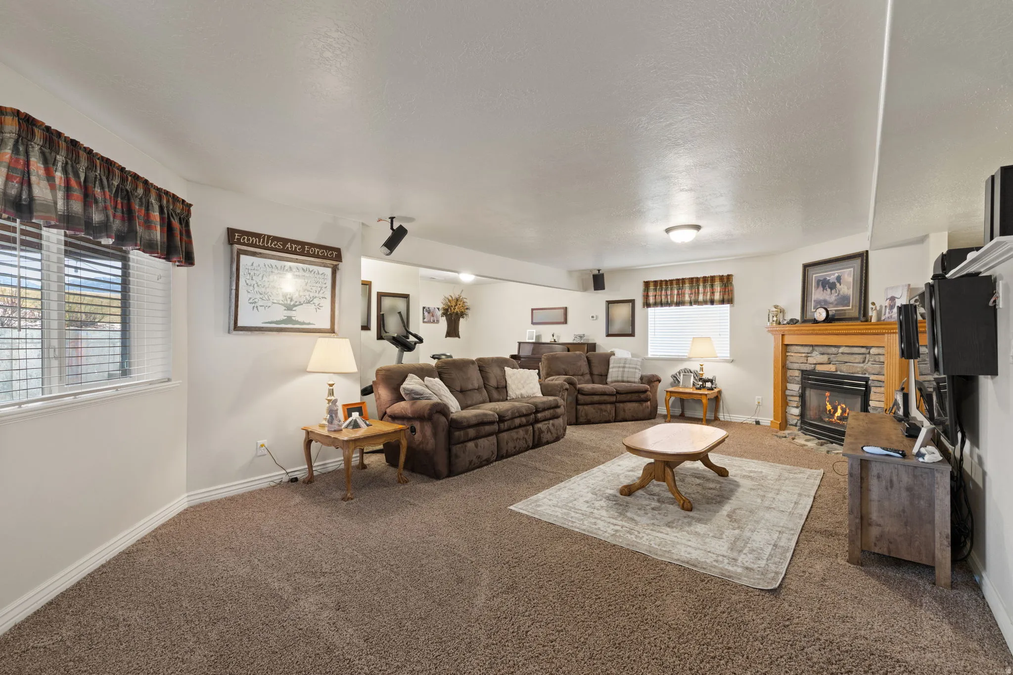 Carpeted interior space featuring a stone-faced fireplace with a wood mantel, recessed lighting, and built-in ceiling speakers