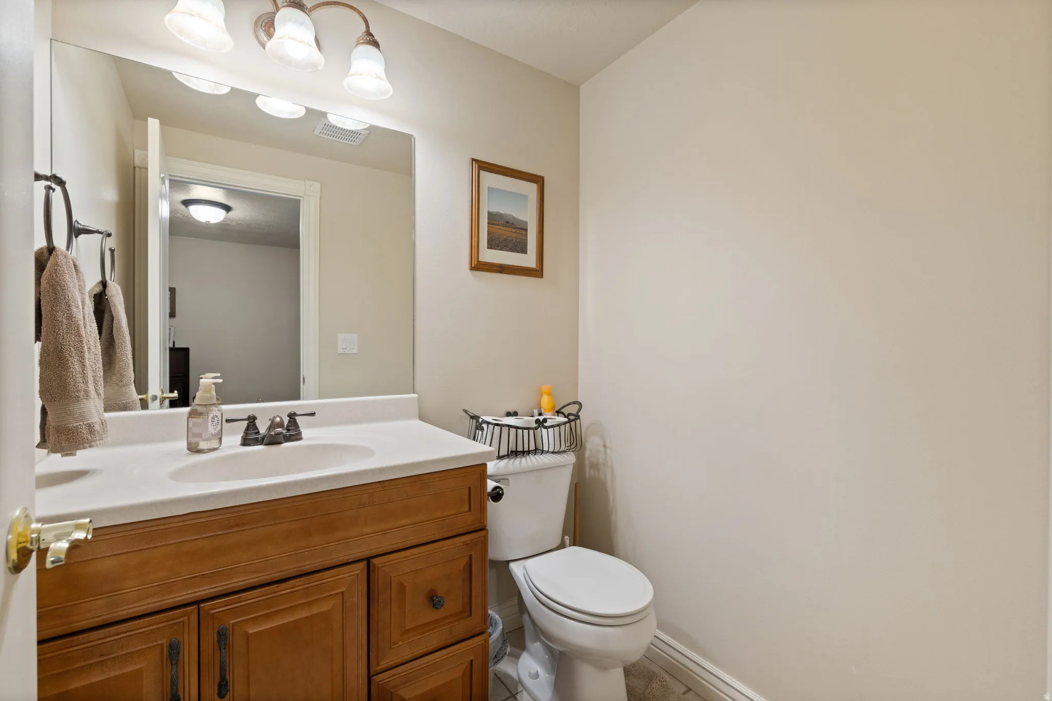 Bathroom featuring a wood-finish vanity with an integrated white sink, a coordinating countertop, and a large wall-mounted mirror