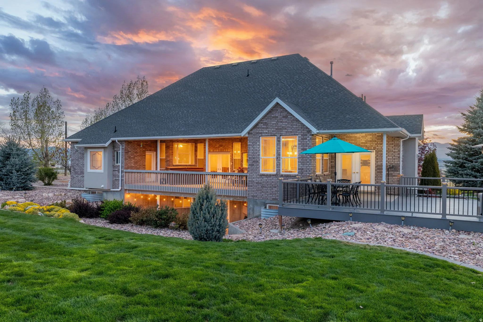 Rear exterior featuring multi-tone brick and stone siding, a dark shingle roof, and a spacious elevated deck with dark railings