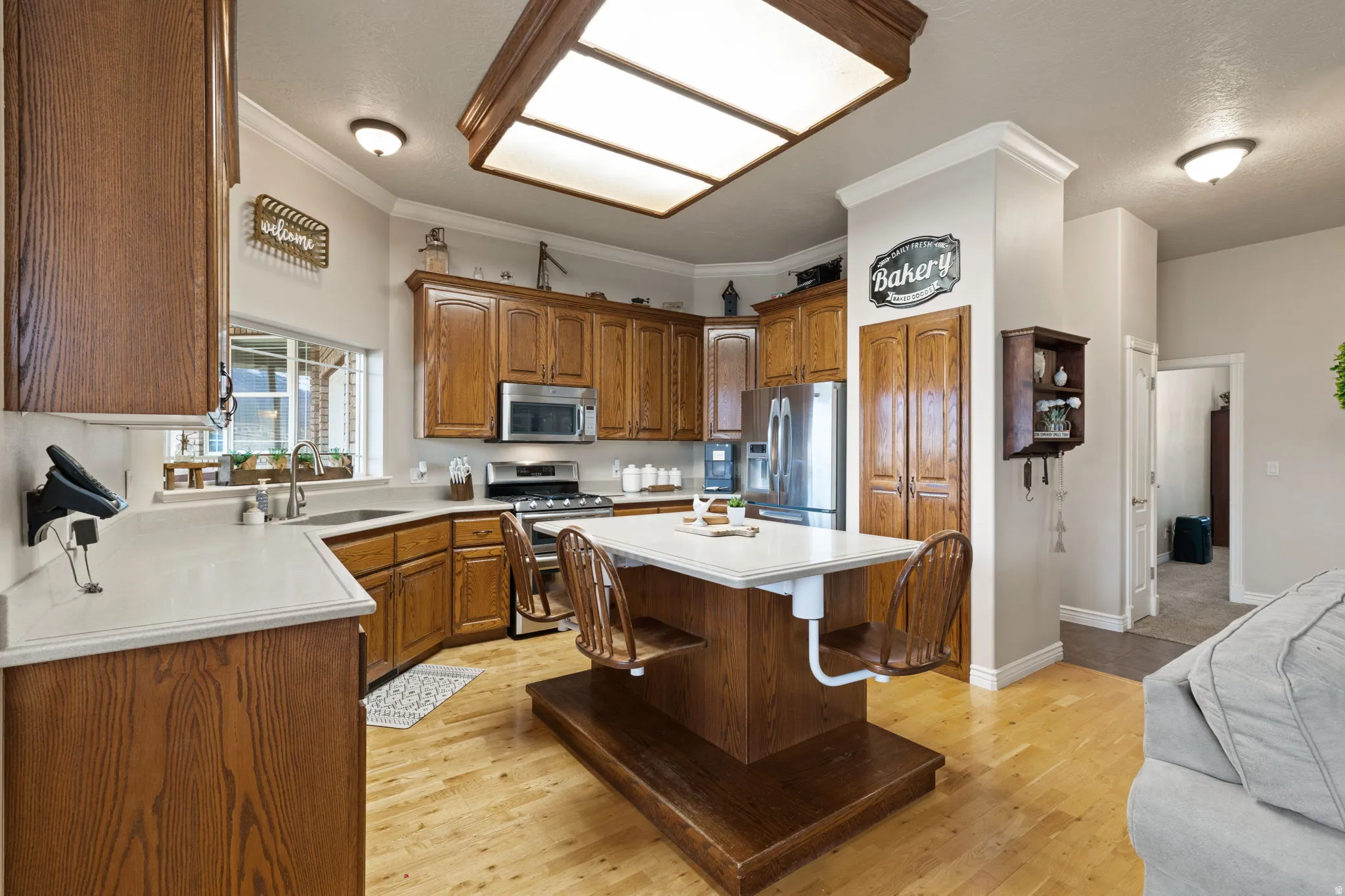 Kitchen featuring wood cabinetry, light-toned countertops, a built-in stainless steel microwave, and wood-finish flooring