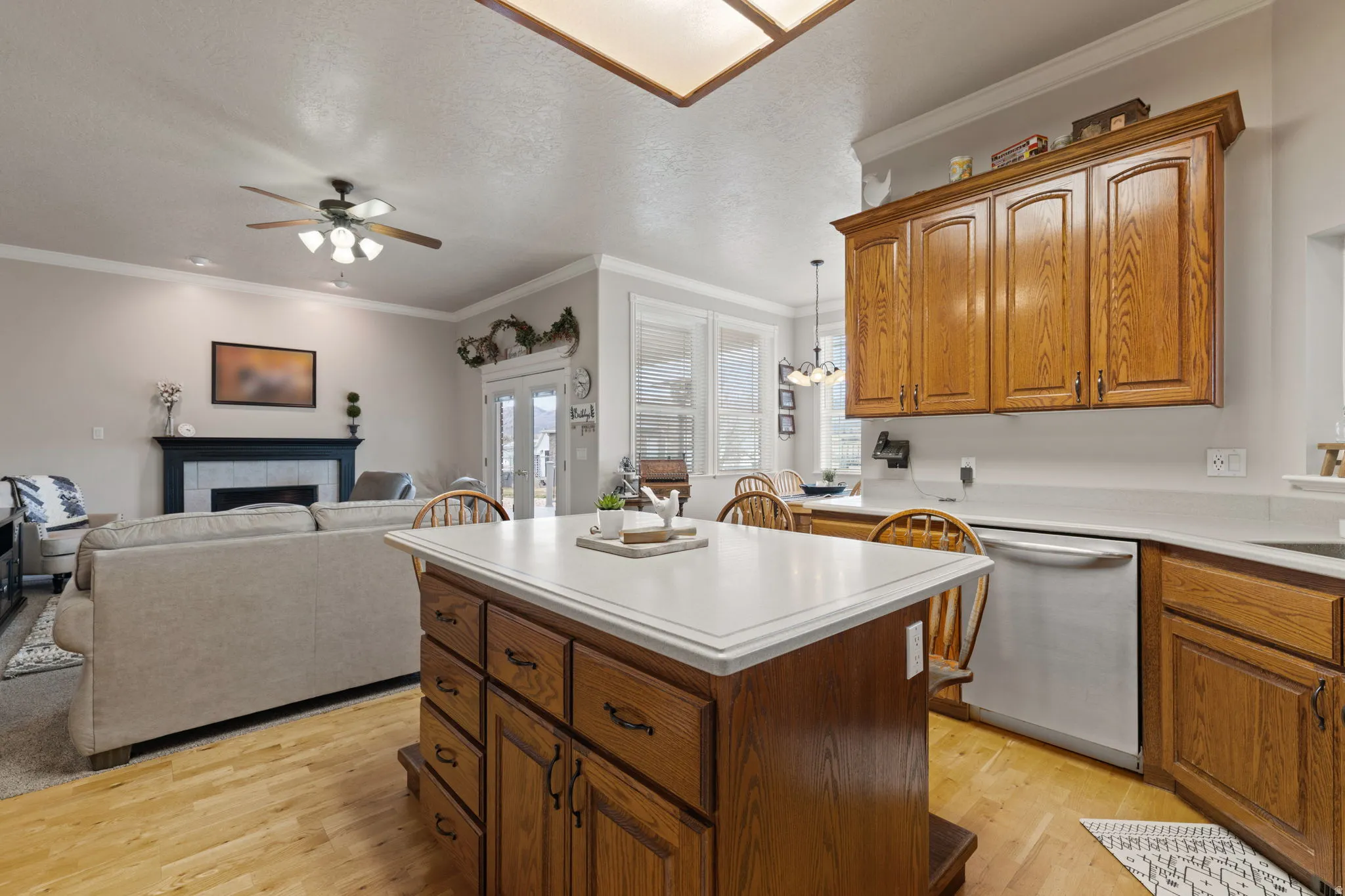 Kitchen island with solid surface countertop, oak cabinetry, stainless steel dishwasher, wood-finish flooring, and crown molding