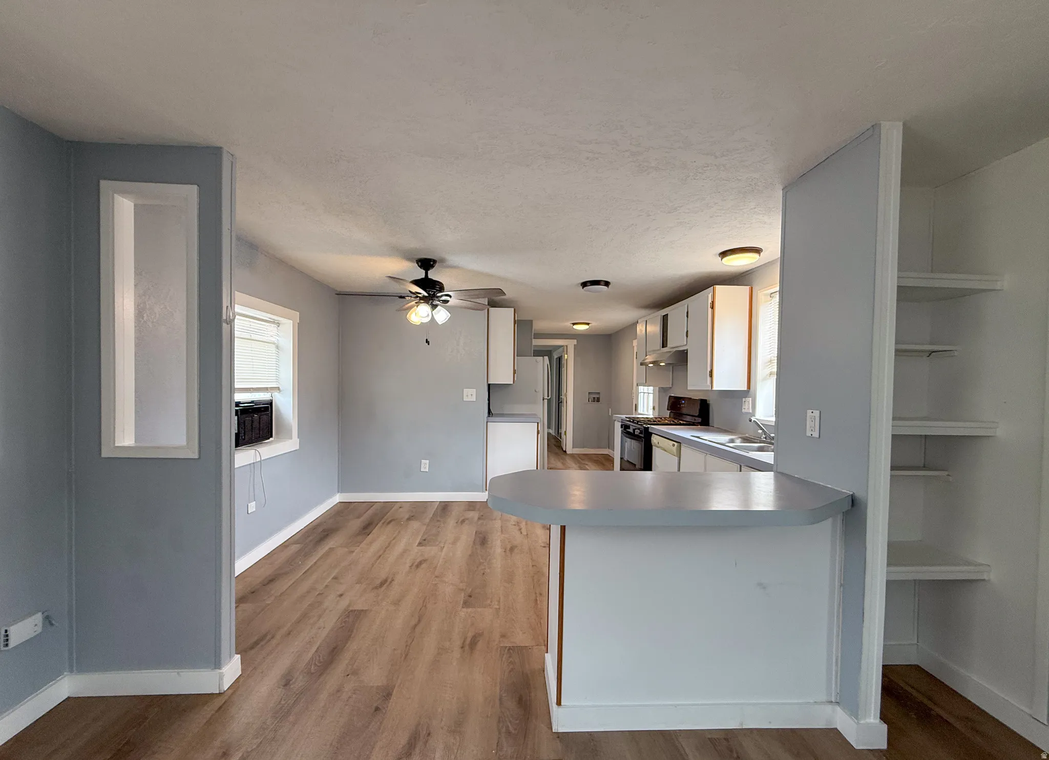 Open concept living area featuring wood-finish flooring, a ceiling fan, and recessed wall niche
