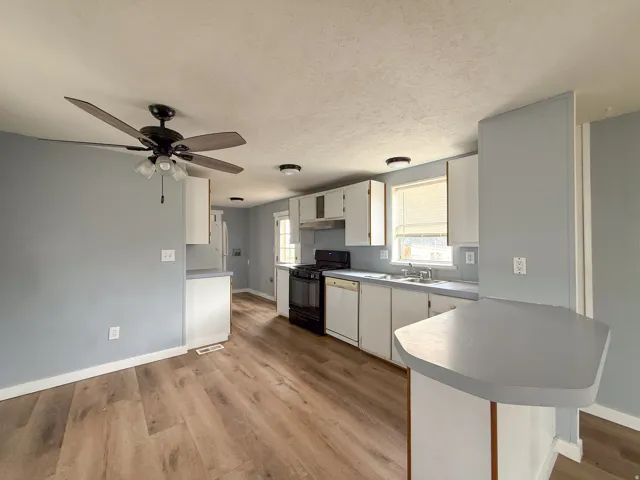 Kitchen featuring light wood-finish flooring, white cabinetry, dark countertops, and a full suite of appliances including a black range and a white dishwasher