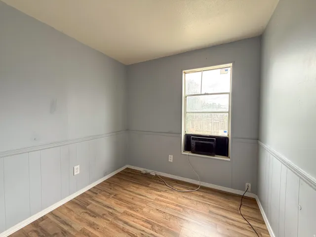 Room featuring wood-finish flooring, light blue walls with beadboard wainscoting, and a window with an integrated air conditioning unit