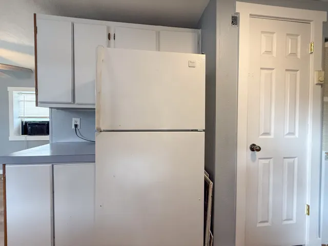 White paneled cabinetry with coordinating hardware, a window with blinds, and light-toned countertops
