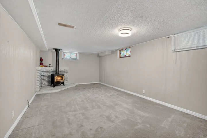 Spacious room featuring a corner wood-burning stove with a white brick surround and hearth, neutral carpeting, and a modern flush-mount ceiling light fixture