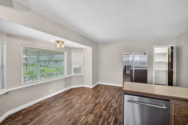 Spacious eating area featuring wood-finish flooring and a wide bay window with blinds