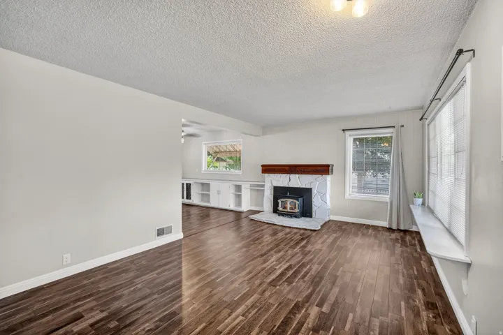 Spacious living area featuring wood-finish flooring, a stone-clad fireplace with a wood mantel, and expansive windows