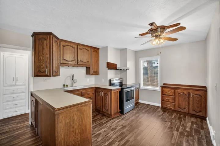 Kitchen featuring wood-finish flooring, wood cabinetry, stainless steel range and range hood, and a built-in white storage cabinet