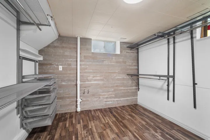 Versatile room featuring wood-finish flooring, a wood-paneled accent wall, a utility sink rough-in, an egress window, and built-in metal shelving