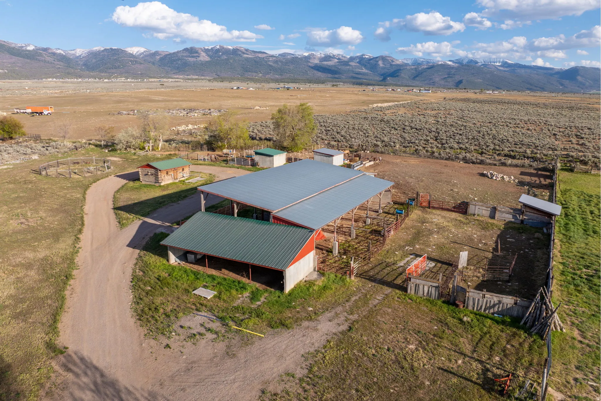 Expansive property featuring a large red barn with a gray metal roof, multiple fenced enclosures, and a dirt driveway
