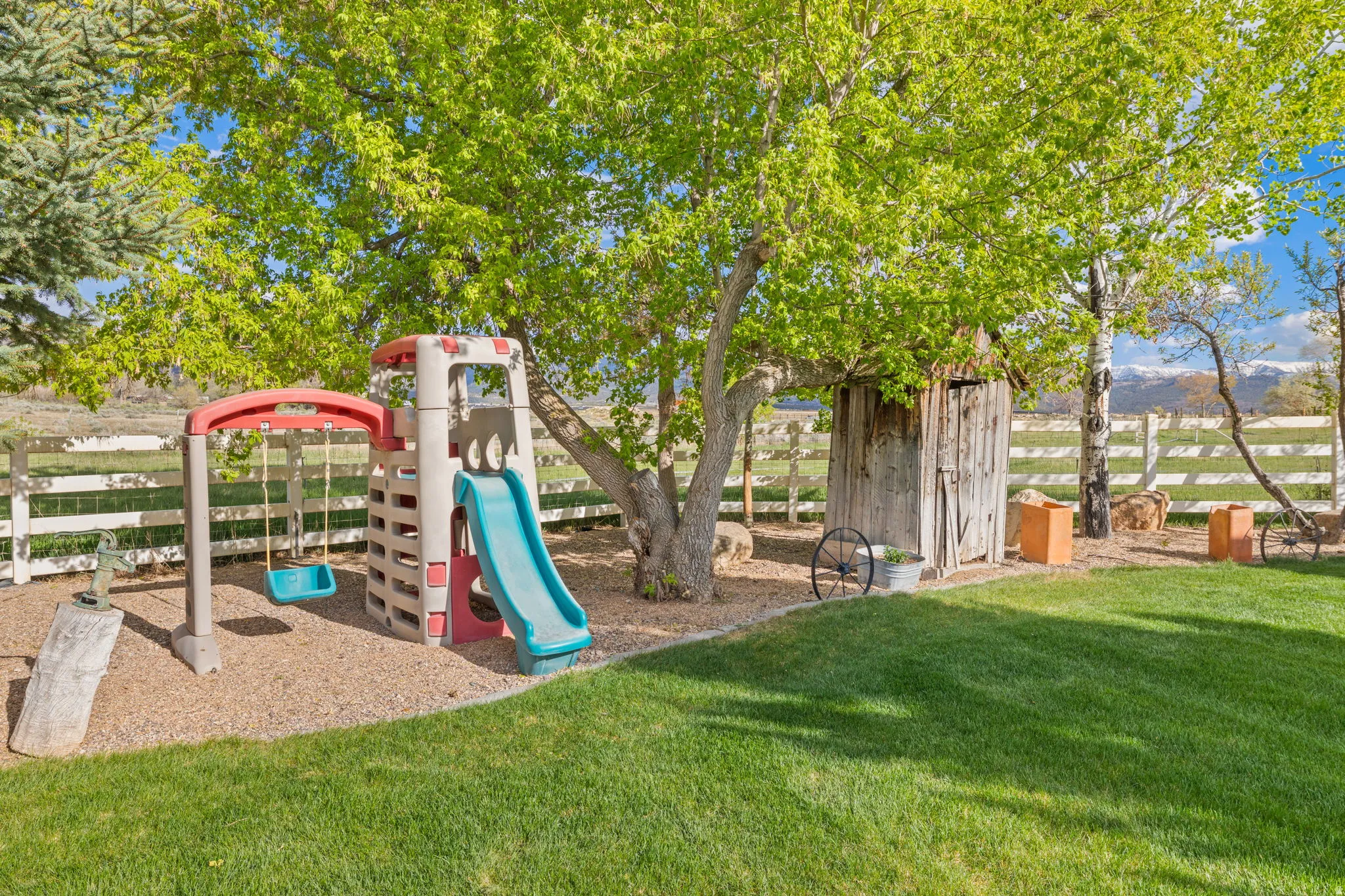 Expansive grassy lawn area featuring mature trees and a white split-rail fence