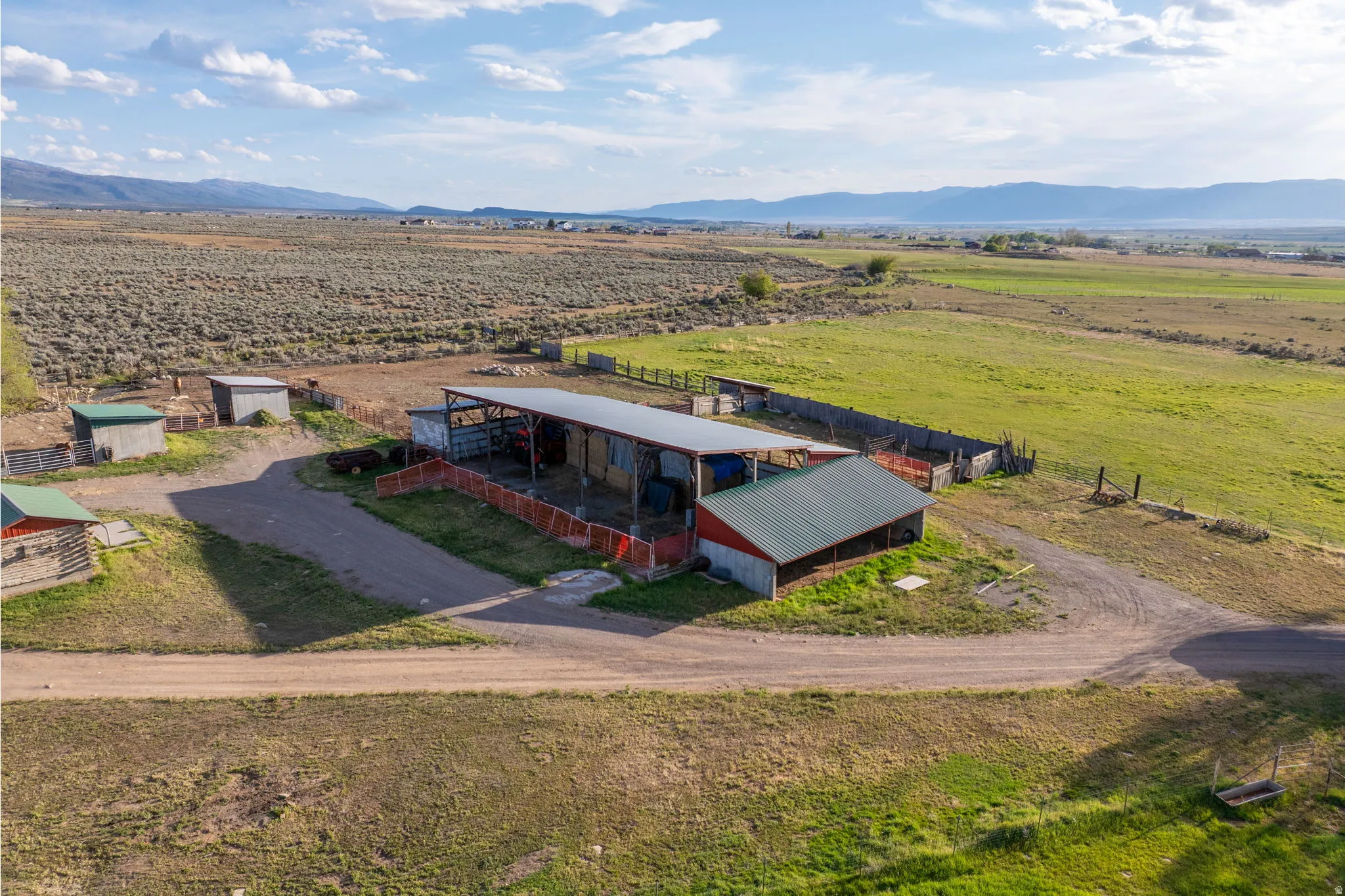 Expansive property featuring multiple outbuildings, fencing, and a large open-sided barn with a metal roof