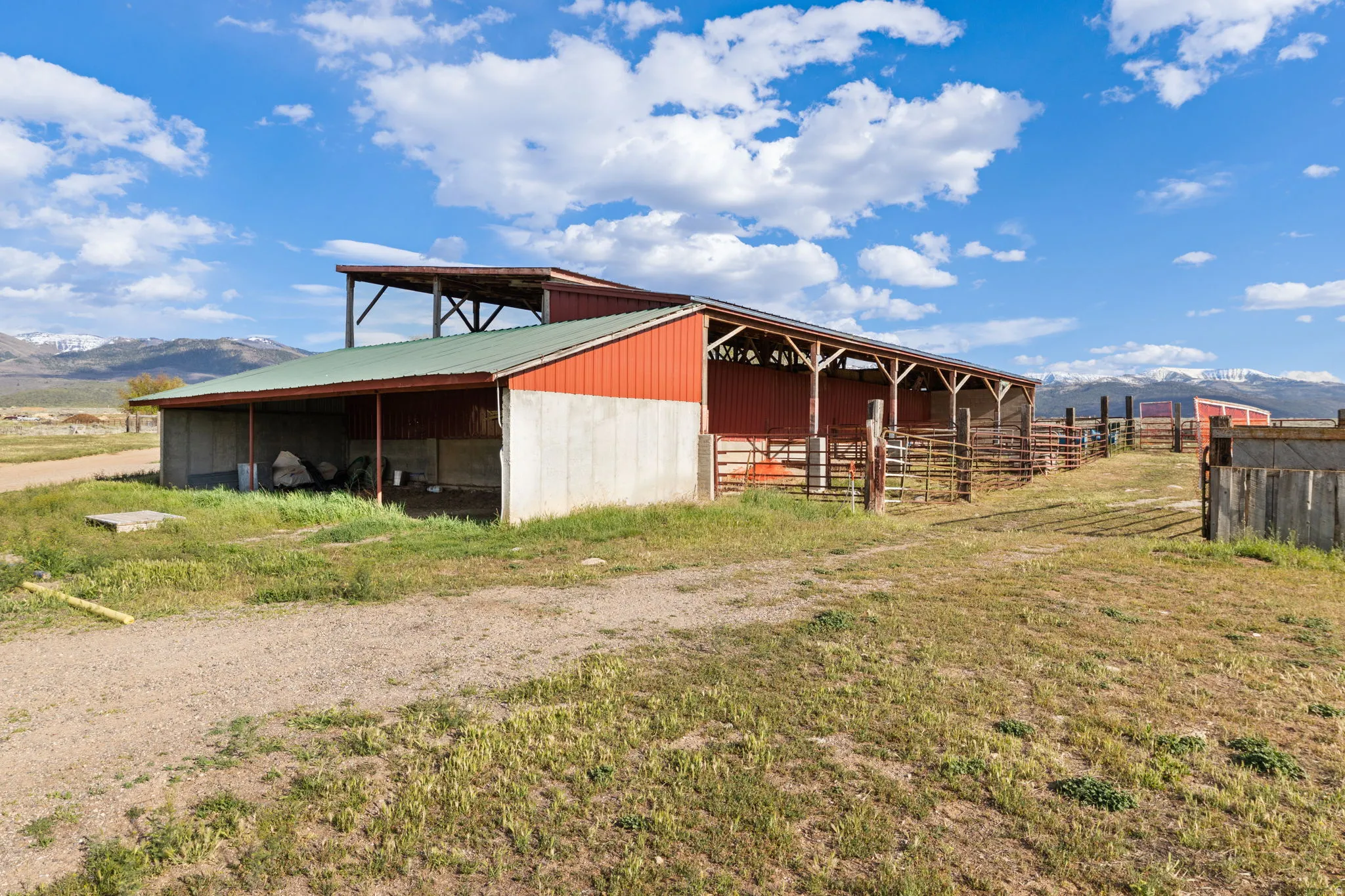 Red metal-sided barn featuring an open-sided shed, a green metal roof, and an attached covered lean-to structure