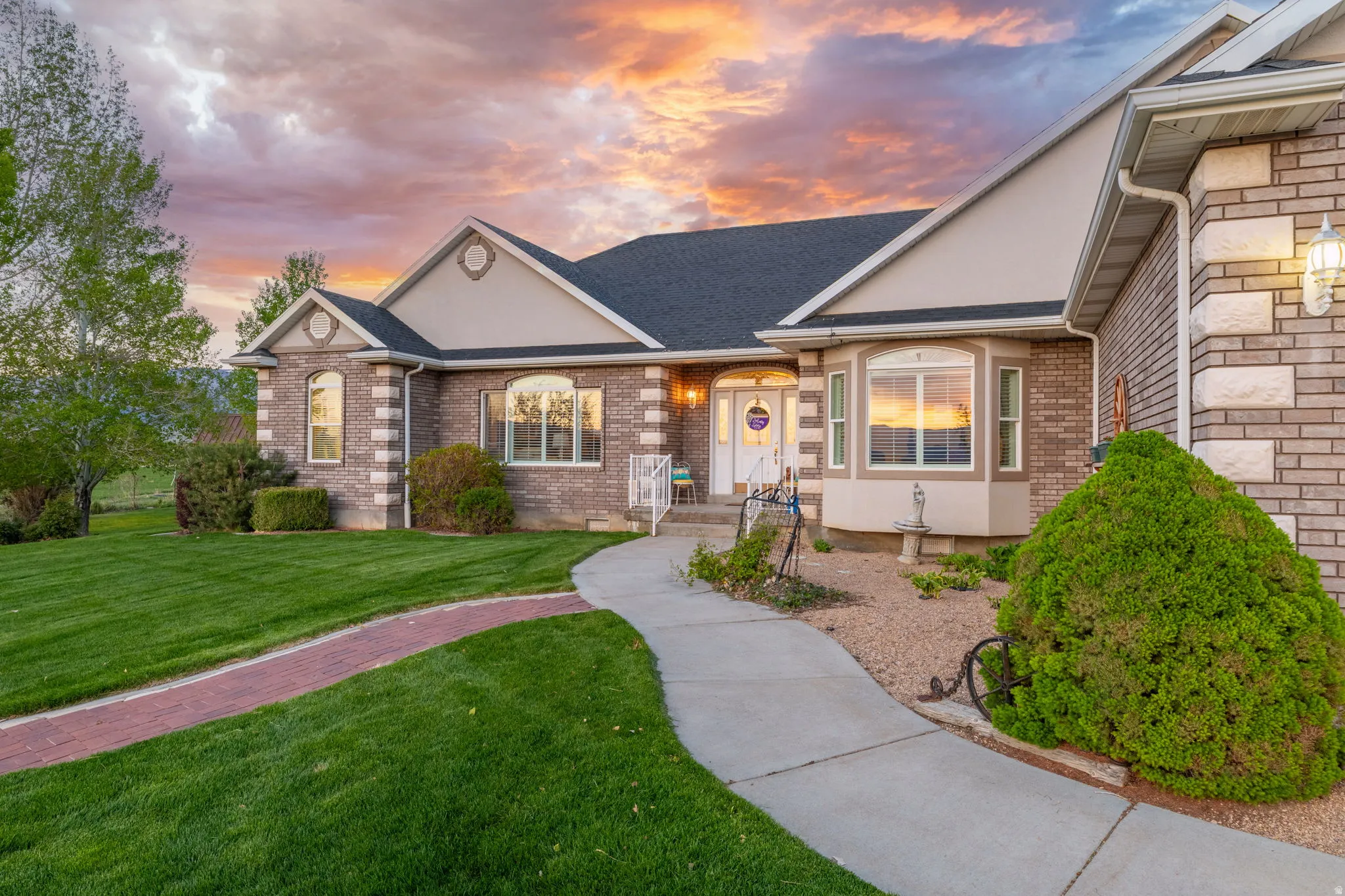 Exterior featuring brick and stone veneer, bay windows, a paved walkway, a manicured lawn, and mature landscaping