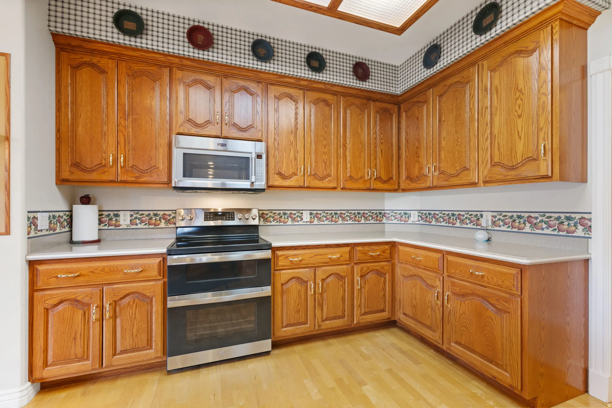Kitchen featuring abundant wood cabinetry, light countertops, stainless steel appliances, and wood-finish flooring