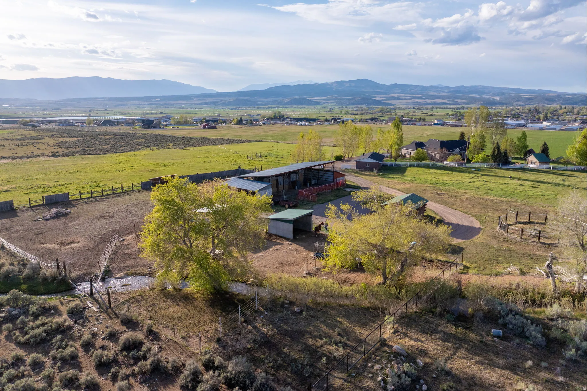 Expansive rural property featuring multiple outbuildings, fenced enclosures, and mature trees on a rolling landscape