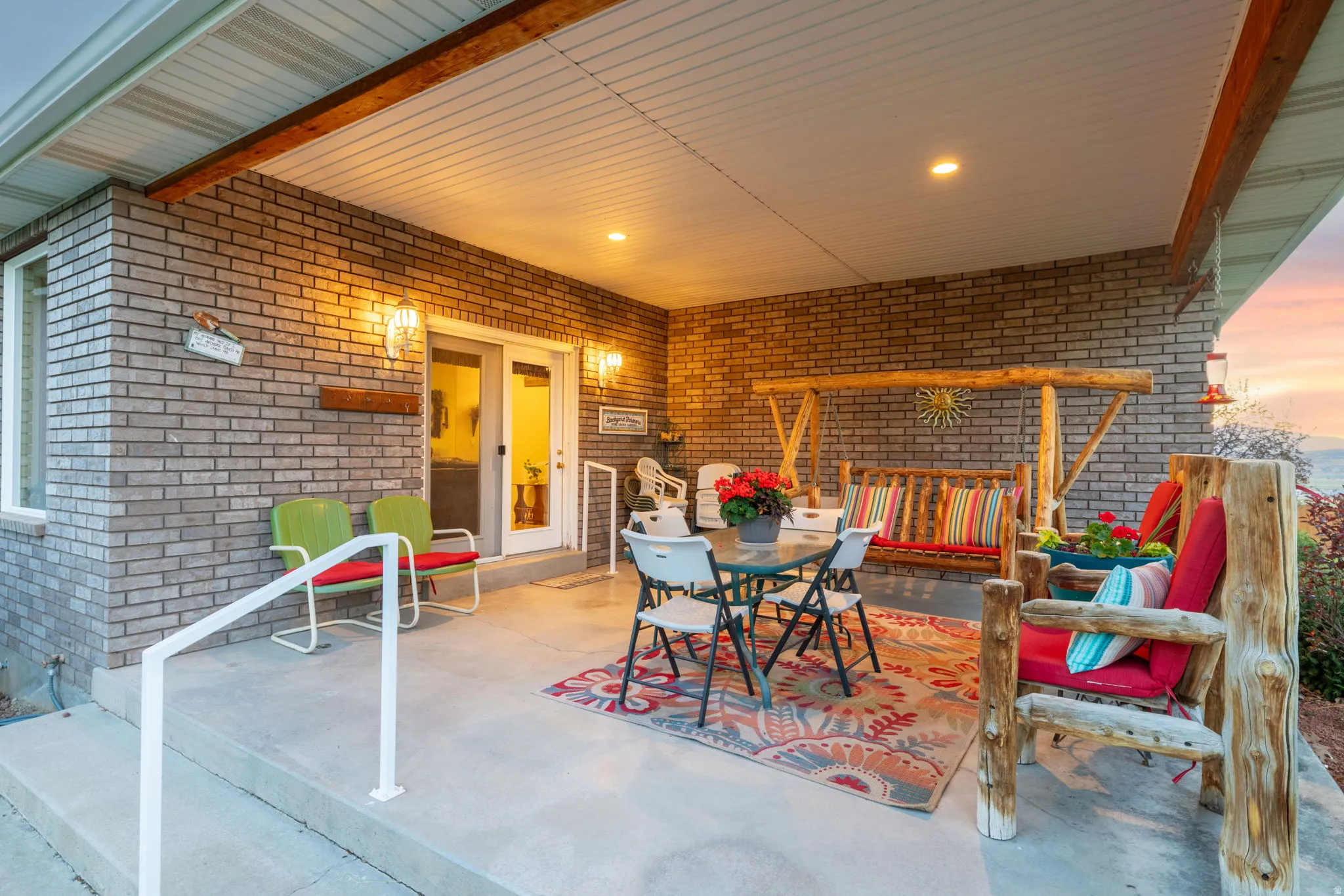 Covered outdoor patio featuring brick siding, concrete flooring, a white railing, recessed lighting, and wall-mounted sconces