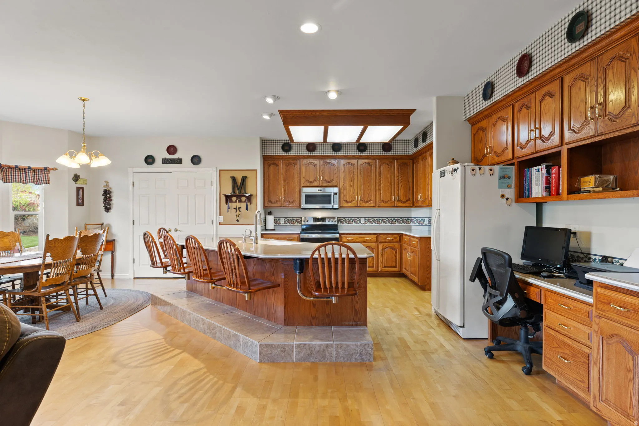 Spacious kitchen featuring warm wood cabinetry, a central island with integrated seating, and light wood-finish flooring throughout