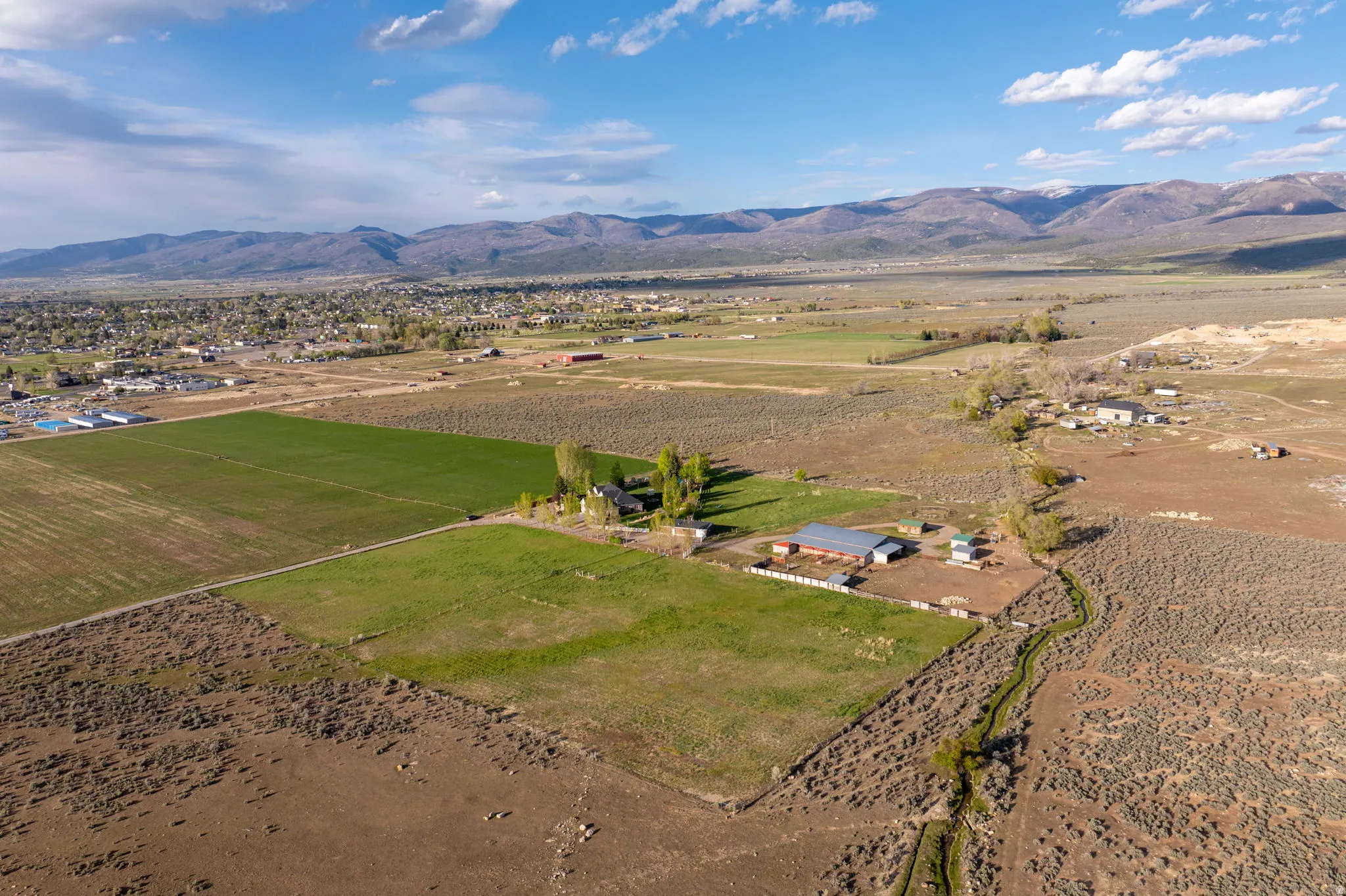 Expansive rural property featuring multiple agricultural fields, a meandering natural waterway, and distant mountain ranges