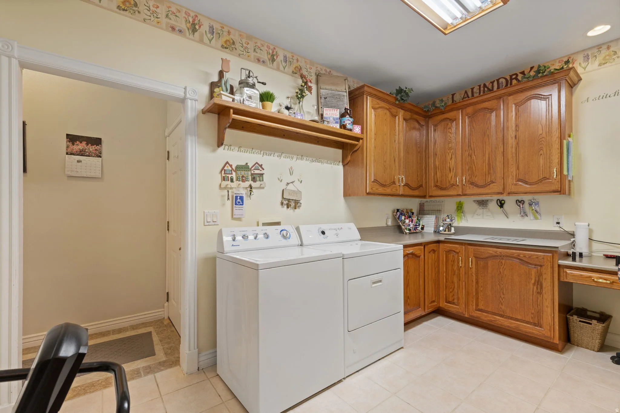 Dedicated laundry space featuring a side-by-side washer and dryer, light wood cabinetry, a built-in countertop, and task lighting